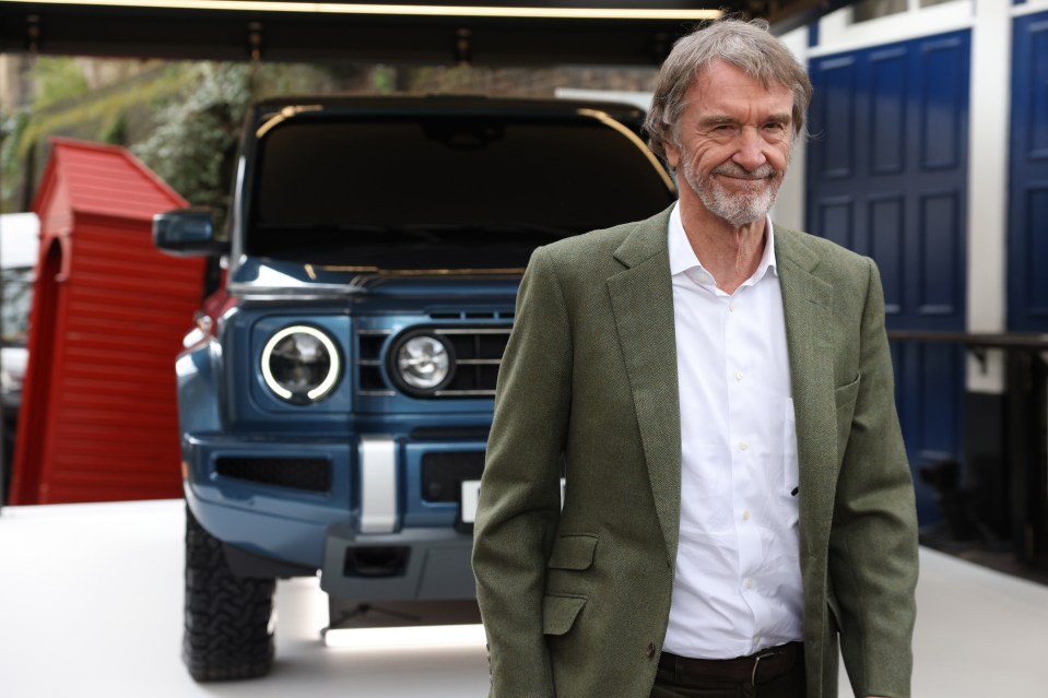 a man in a suit stands in front of a blue car