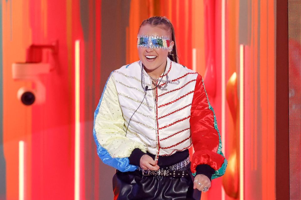 JoJo Siwa on Celebrity Big Brother, wearing a colorful jacket and mask.