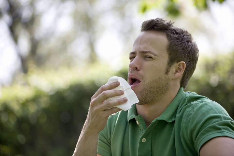 A young man outdoors, sneezing
