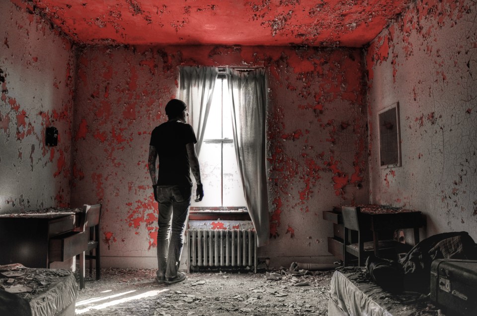Seph stands alone in the remains of a crumbling home. A suitcase, bed and table are all that remain in the bedroom