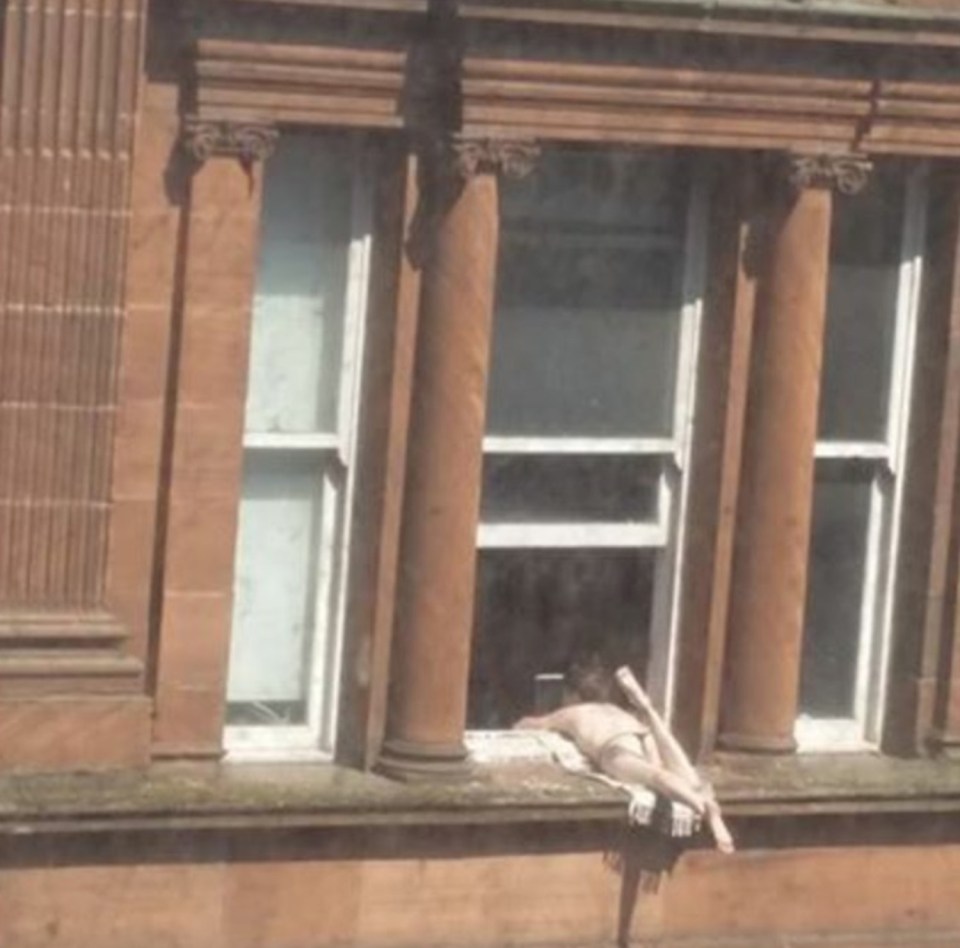 The cheeky sunbather was topless as she dangled her legs out the third-floor window