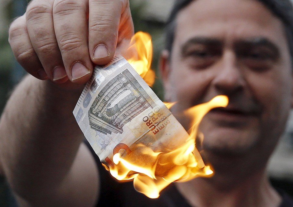 An anti-austerity protester burns a euro note during a demonstration outside the European Union (EU) offices in Athens