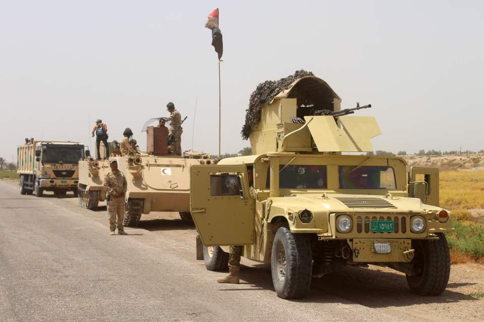 Iraqi government forces stand next to their vehicles as they hold position southwest of Fallujah