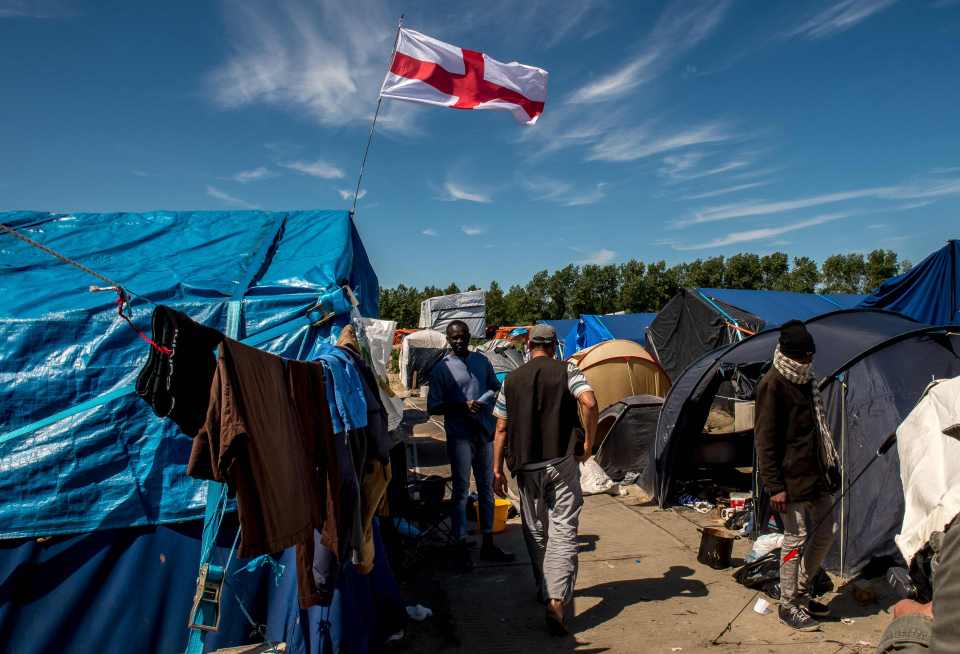 Migrants walk past a flag of England inside the 'Jungle' camp in wake of Brexit