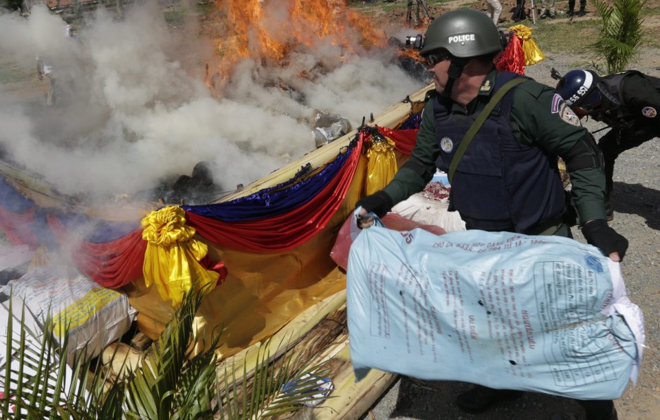 Cambodian police officer throws a bag of marijuana on a fire 
