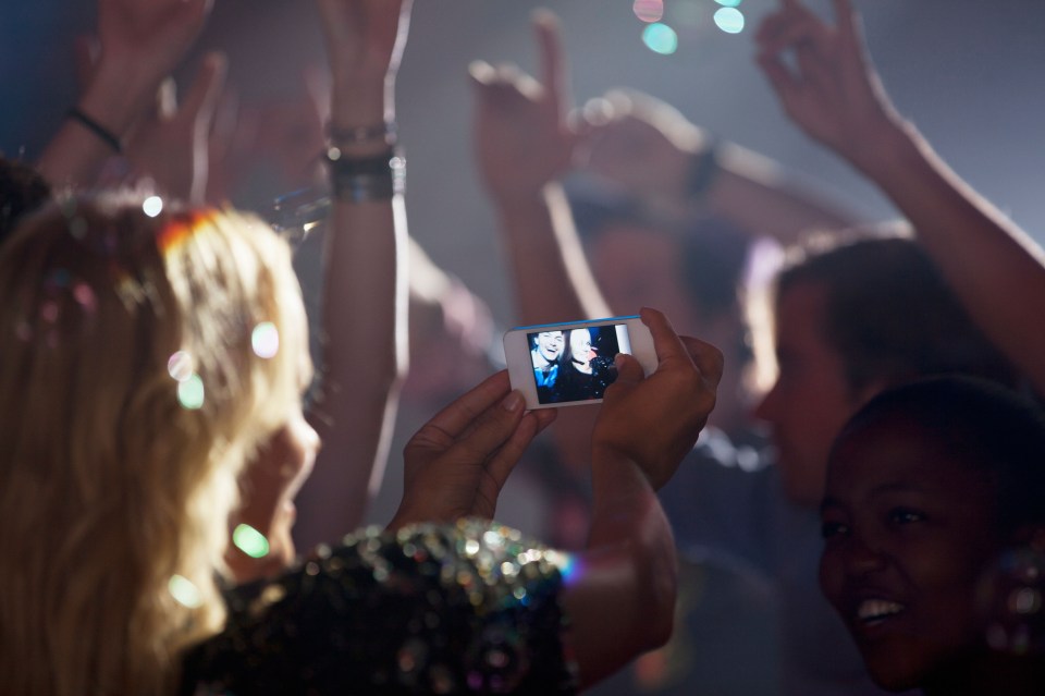 Woman with camera phone photographing friends on dance floor of nightclub. Image shot 2012. Exact date unknown.