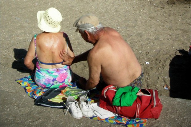 An Elderly Man Spreads Sunscreen On The Back Of A Woman