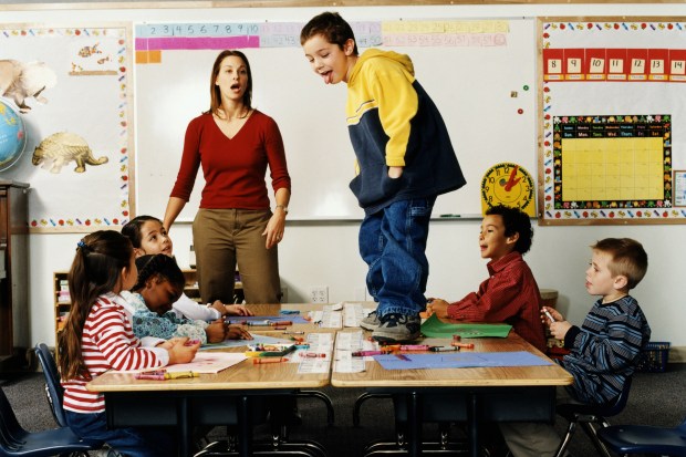 Boy (5-7) standing on desk in front of class