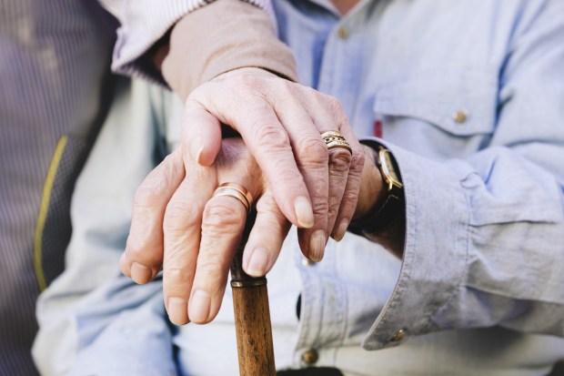 Close-up of old mans and womans hands resting on a cane