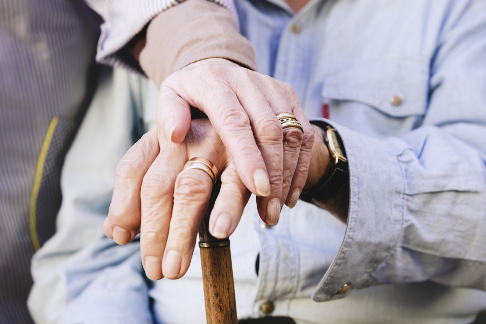 Close-up of old mans and womans hands resting on a cane