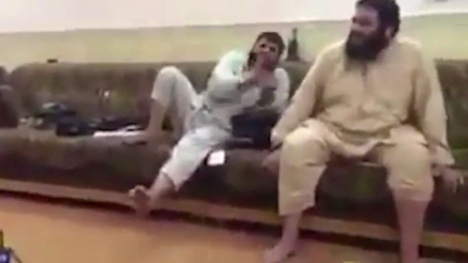 Two suspected ISIS jihadis lounge around as a woman can be heard being raped off camera