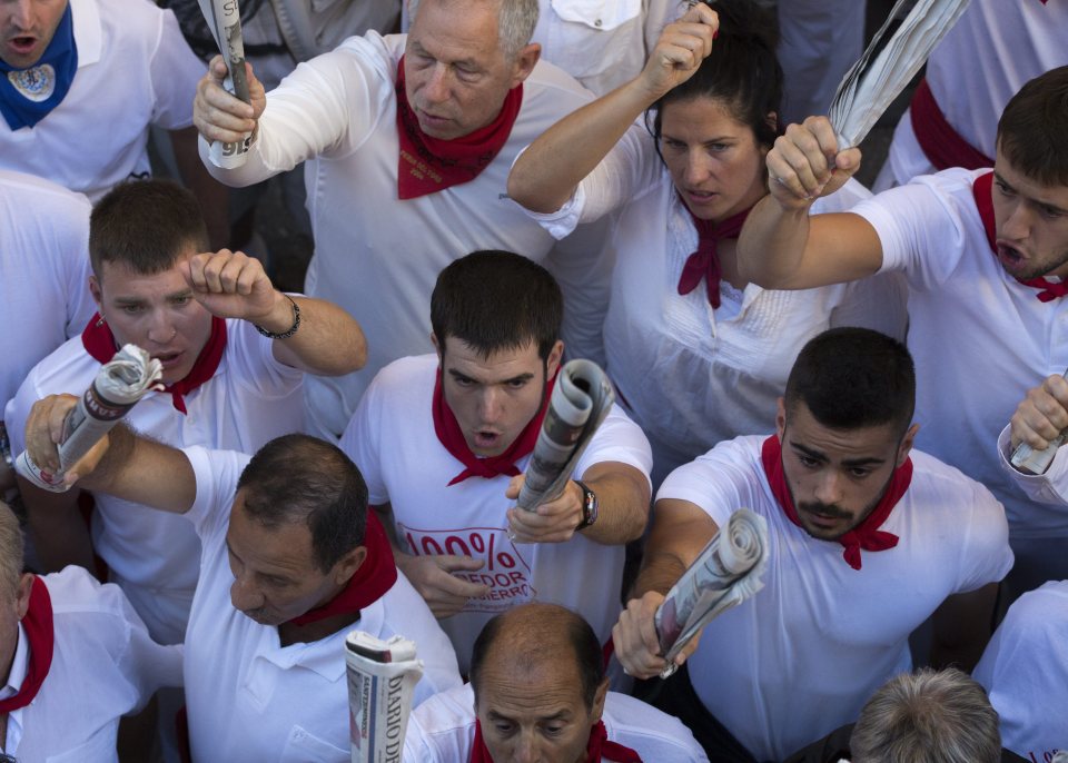 Bull runners point rolled-up newspapers at a small san Fermin statue with candles inside a niche on the Cuesta Santo Domingo as they sing a song to the saint to protect them before the start of the morning's bull run