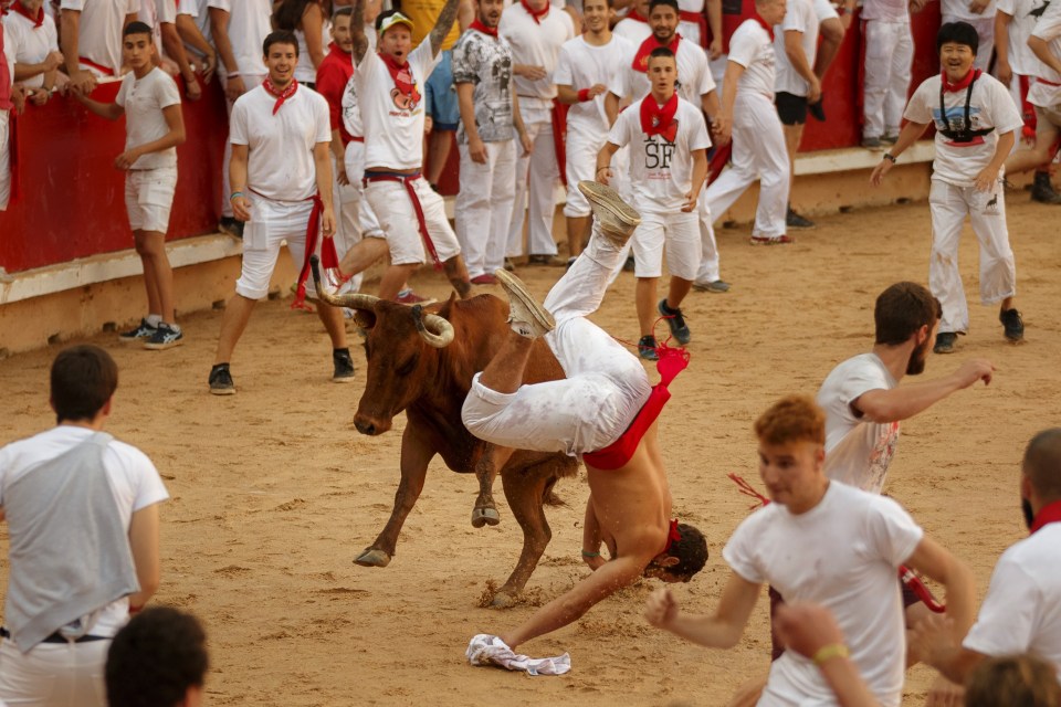 One runner is pushed head over heels by a charging bull as others scramble away from the scene