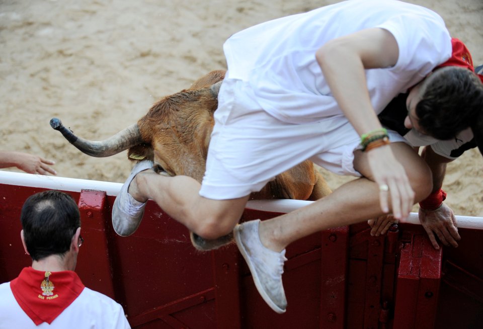 A runner tries to escape the raging bull, clambering over a barrier as it head butts him