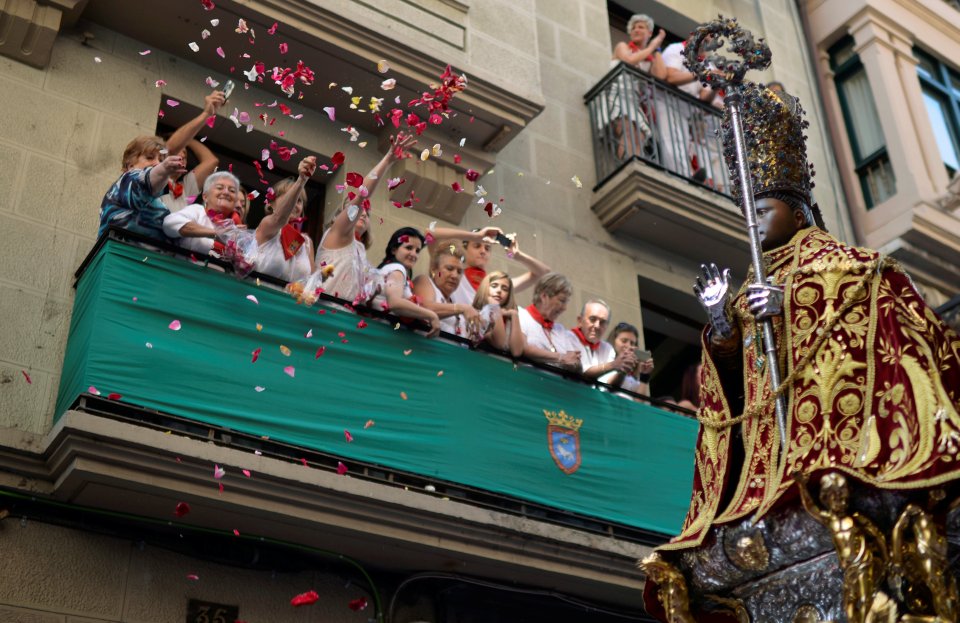 A woman throws flowers down into the street at the statue of San Fermin as it passes