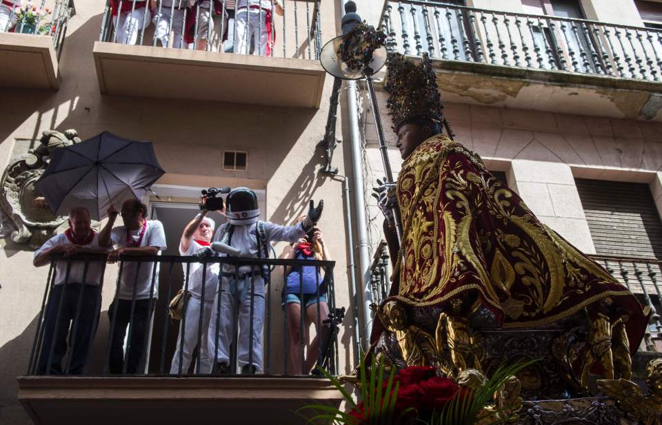 A spectator in an astronaught suit watches from a balcony as the efidgy of San Fermin is carried through the centre of Pamplona
