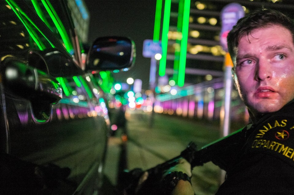 Sweating . . . Police officer James Dylan Smith takes cover behind a car wit his gun during the chaos in Dallas