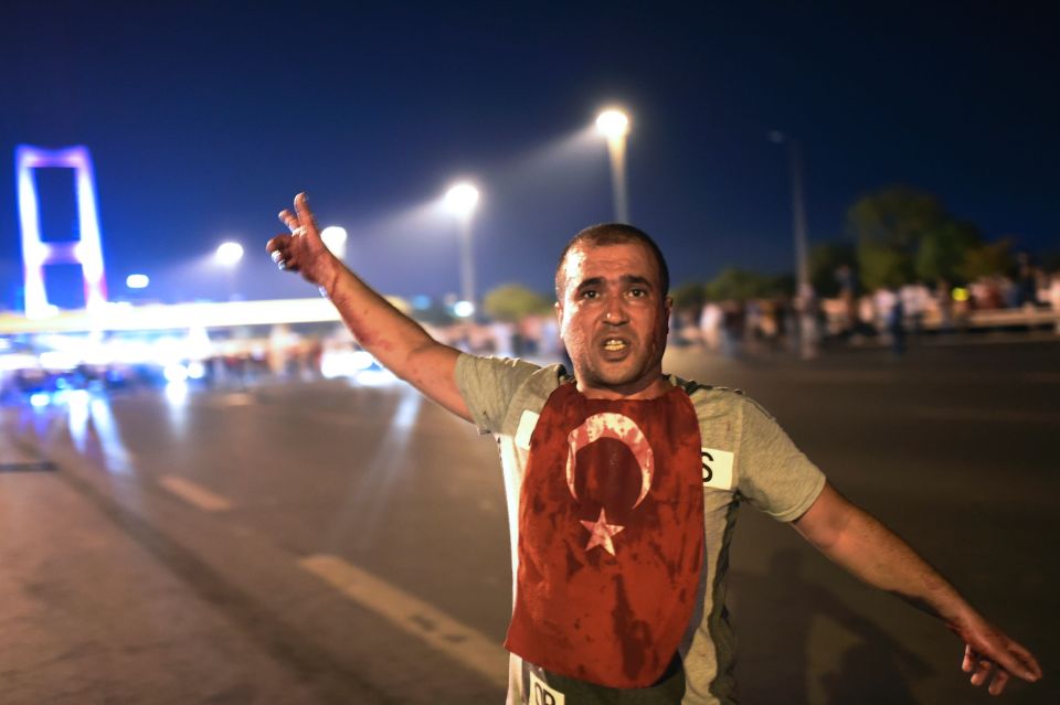 A man covered in blood, wearing the Turkish flag, stands in front of the Bosphorus bridge