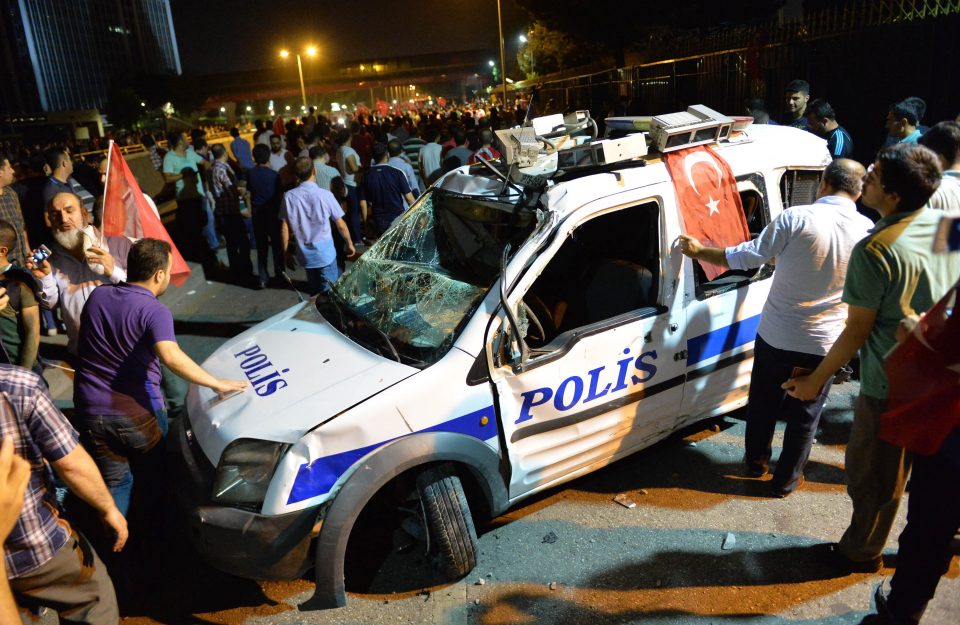 People gather near a destroyed police car with 17 police officers killed in an attack