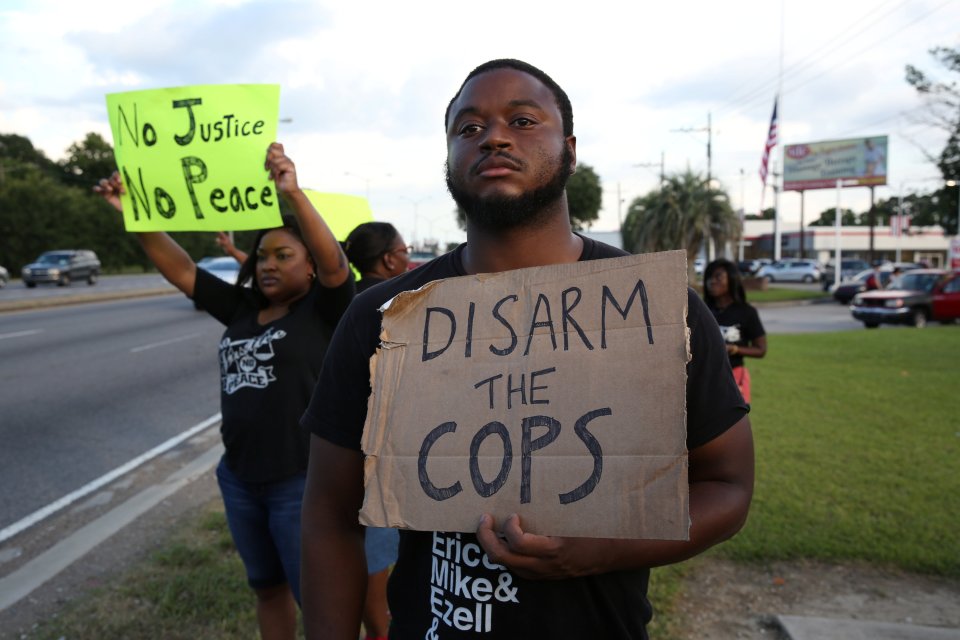 Activist Matthew Kincaid holds a sign that reads "Disarm the cops" as he protests the killing of Alton Sterling by police officers in Baton Rouge, Louisiana