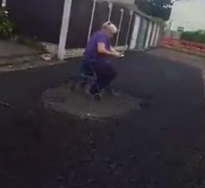 The elderly woman reads a book while surrounded by the newly-laid ashphalt