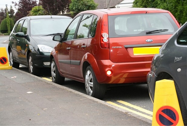 Double yellow lines are painted in between parked cars on Clink Road, Frome