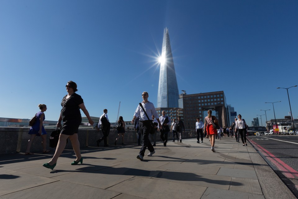Commuters walk to work over London Bridge as the sun reflects on the London Shard 