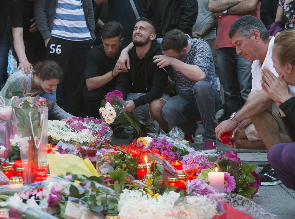 Devastated . . . mourners gathered behind flower tributes at the site where nine people were brutally murdered 