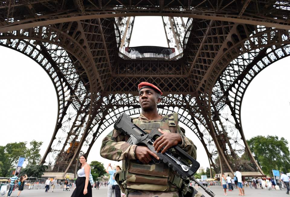 An armed soldier guards the Eiffel Tower, an iconic landmark in Paris
