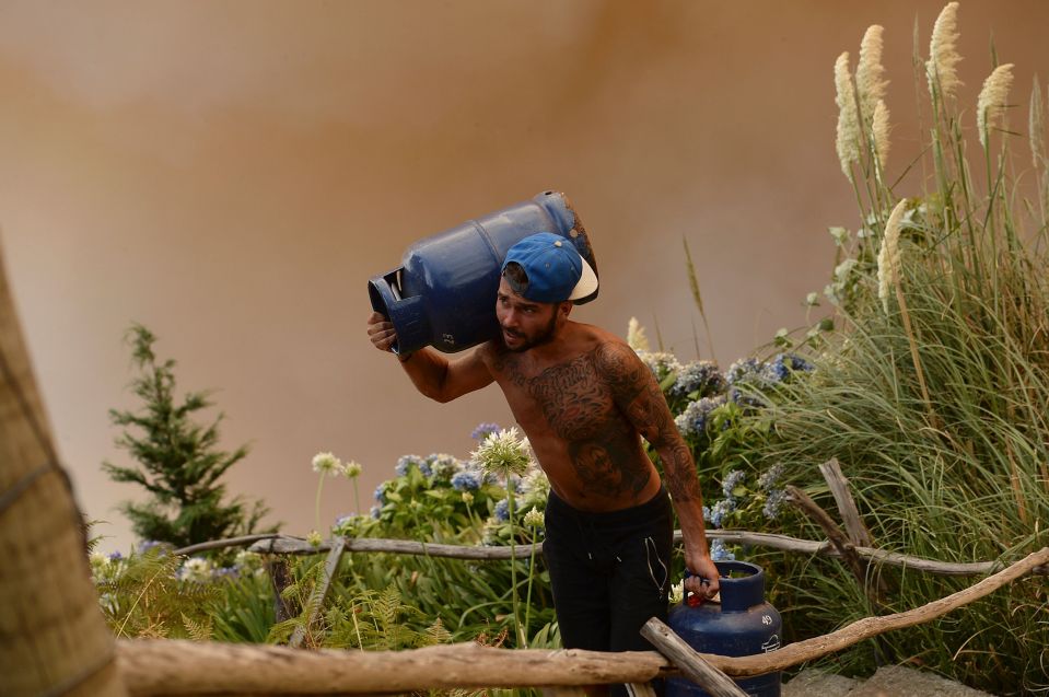  A man can be seen carrying gas cylinders away from the flames at Curral dos Romeiros, Funchal 