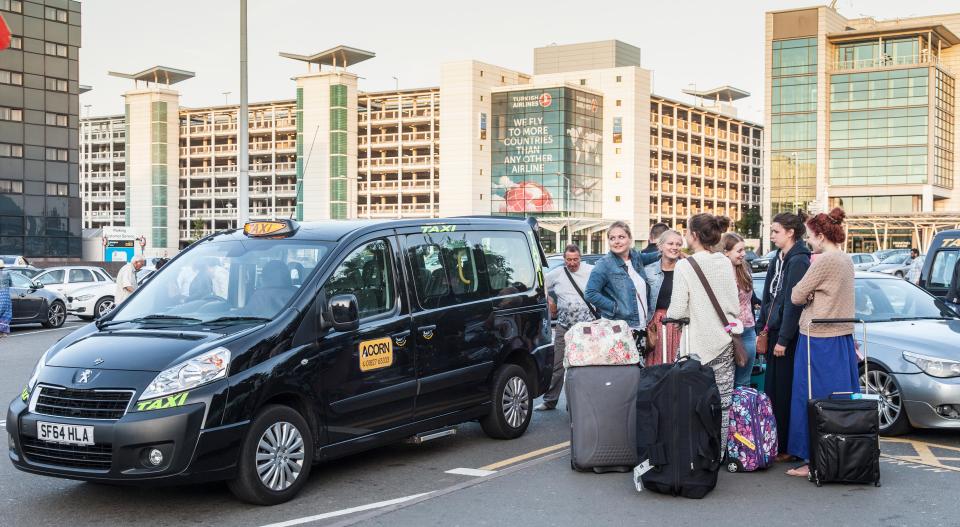 Passengers with luggage standing at a taxi rank outside the arrivals lounge of Birmingham Airport, England, UK