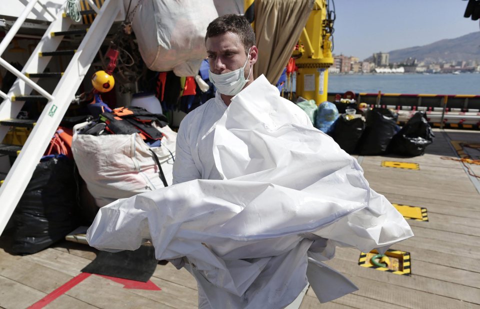 An aid worker appears to carry a small body covered in a white sheet as they rescue migrants from the Mediterranean 