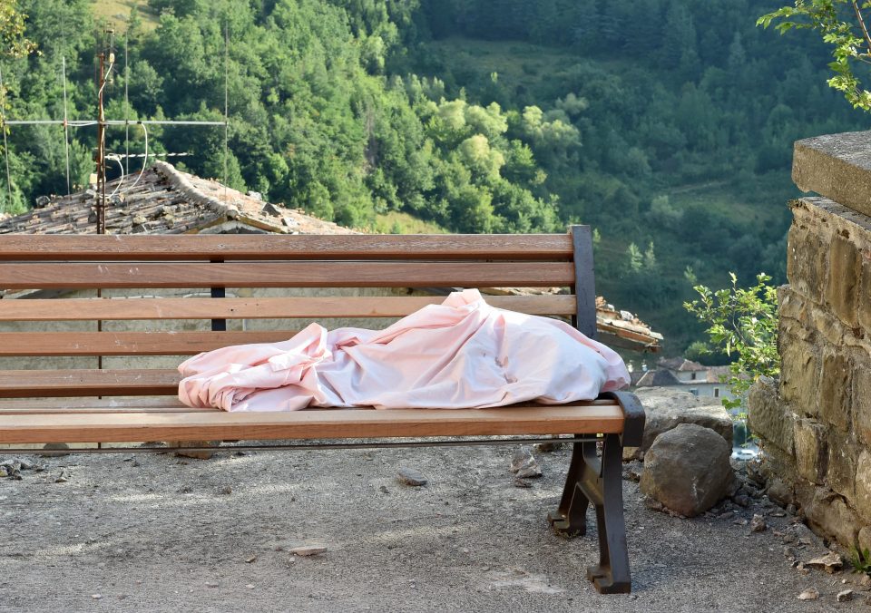 The body of a young victim lies cover by a blanket on a bench in the village of Arquata del Tronto