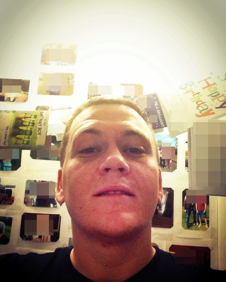 Baillie smiles at the camera with the wall behind him covered in photographs