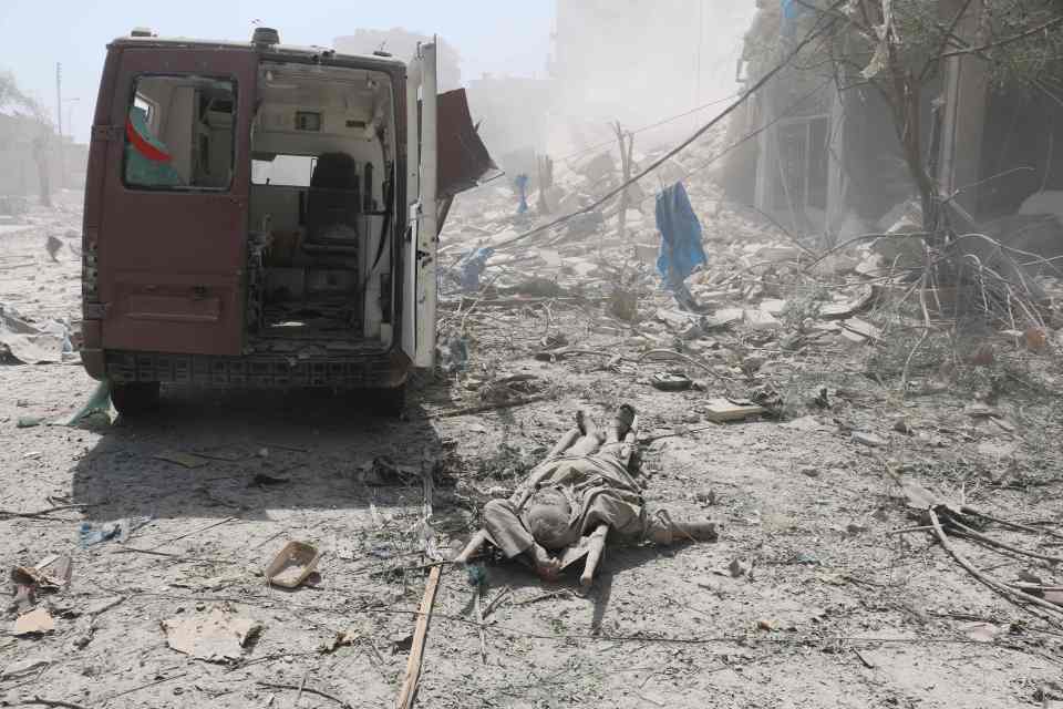 A corpse lies behind a damaged ambulance after a second bomb struck when medics arrived