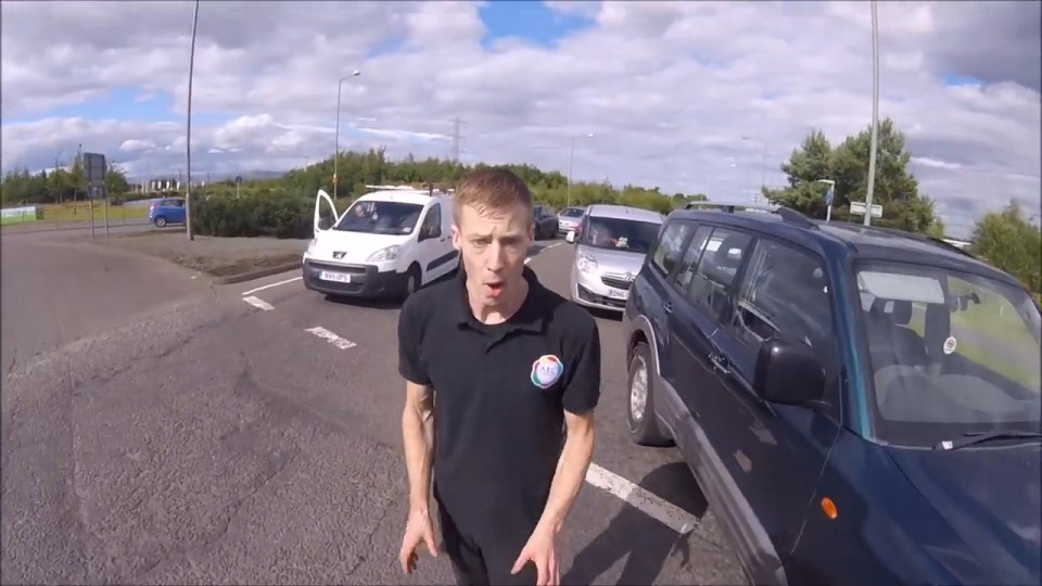 After appearing to get pushed off his bike, the motorcyclist follows the man back to his car