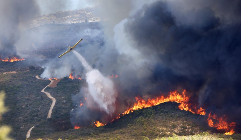 A plane drops water over the fire on the dry hills