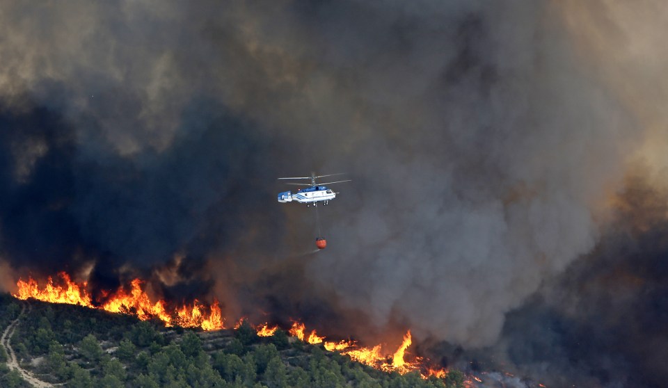 A fire fighting helictoper drops a bucket of water over the fires