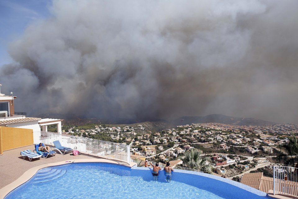 Two people watch the wildfire from a pool as it threatens houses in Benitatxell near Alicante