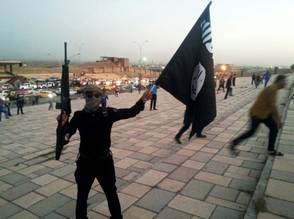 A fighter of ISIL holds a flag and a weapon on a street in Mosul
