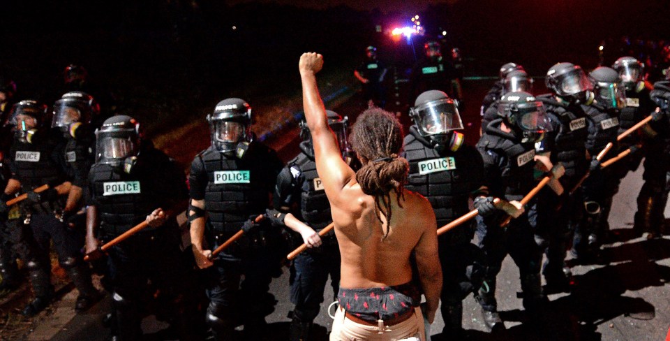 A protester stands with his left arm extended and fist clenched in front of a line of police officers in Charlotte