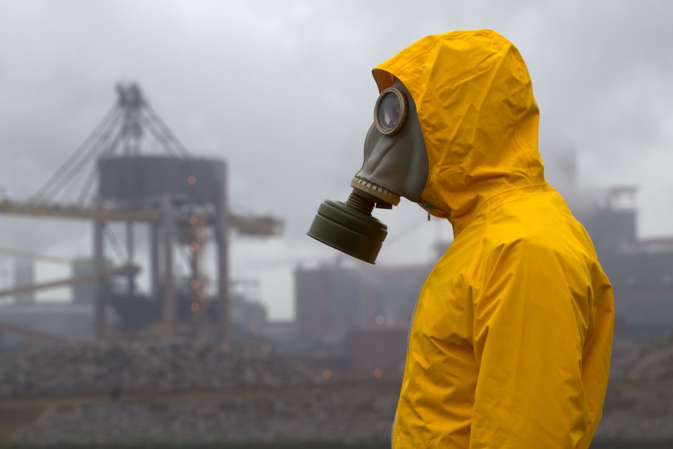 Man wearing gas mask standing in front of factory. Frontal shot.