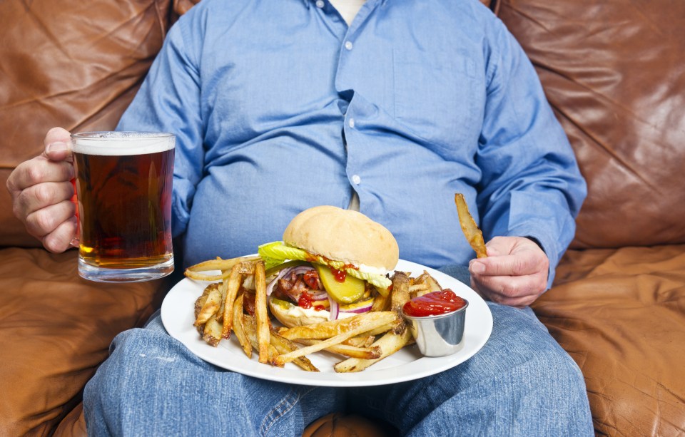overweight man sitting on an old couch with a very large unhealthy meal