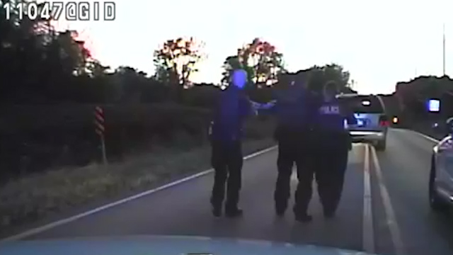 After he walks towards the vehicle followed by a female officer, three male officers immediately surround him