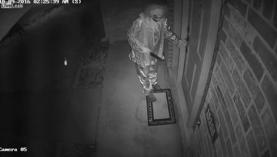 The creepy clown can be seen rattling the front door of the home - with the huge knife in his other hand