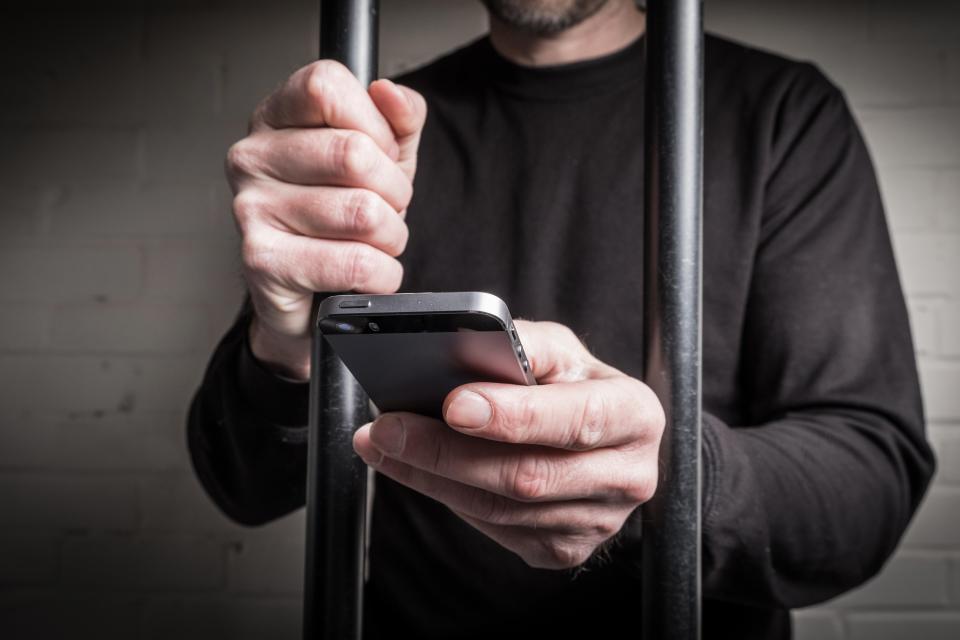 A prisoner in prison using a mobile phone behind bars in a cell. Image shot 02/2016. Exact date unknown.