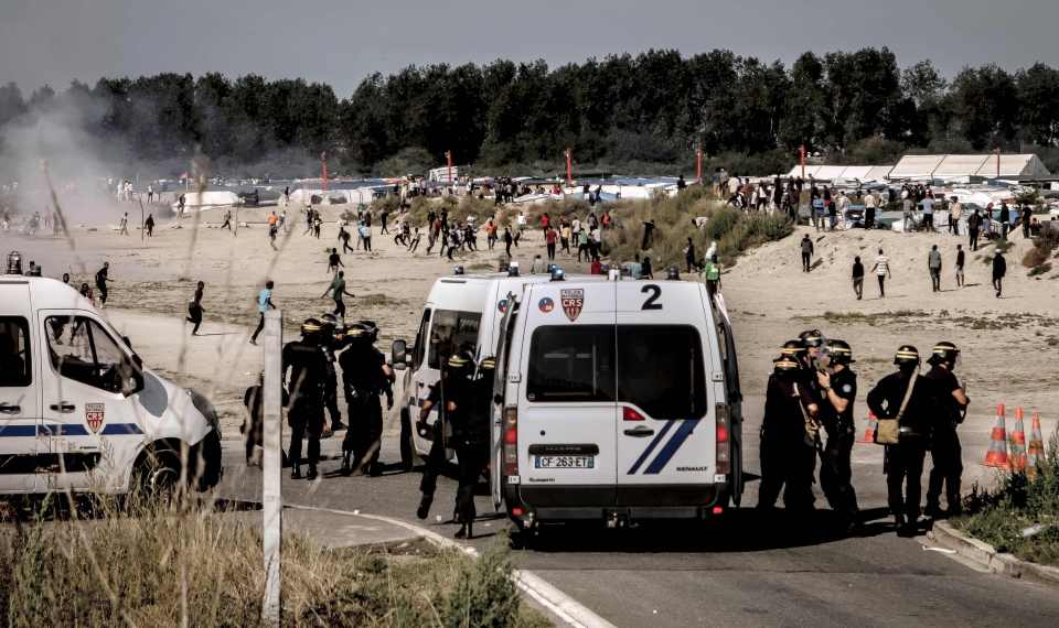 Riot police disperse migrants trying to get into trucks heading to the UK