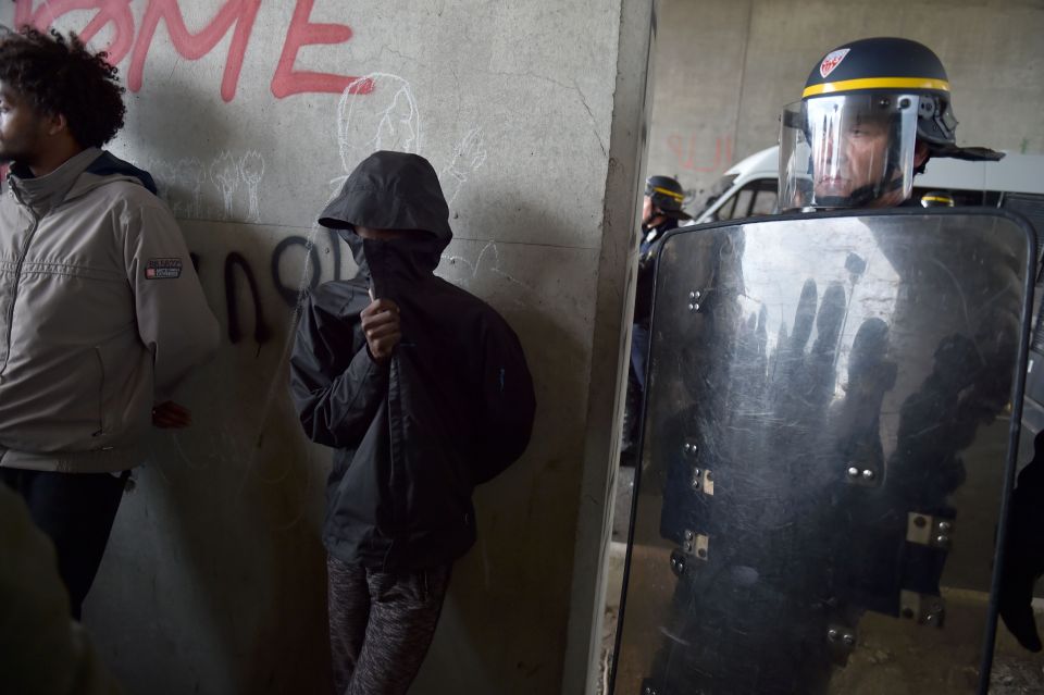 A participant covering his face stands next to a French anti-riot policeman