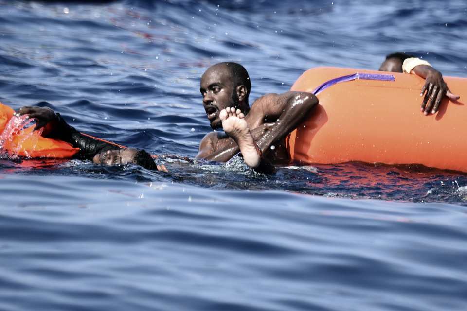 A migrant in water clinging on to a float while waiting to be rescued