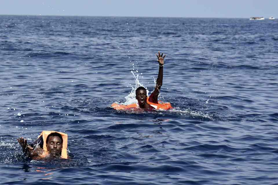 Migrants gesture towards the rescue ship for help